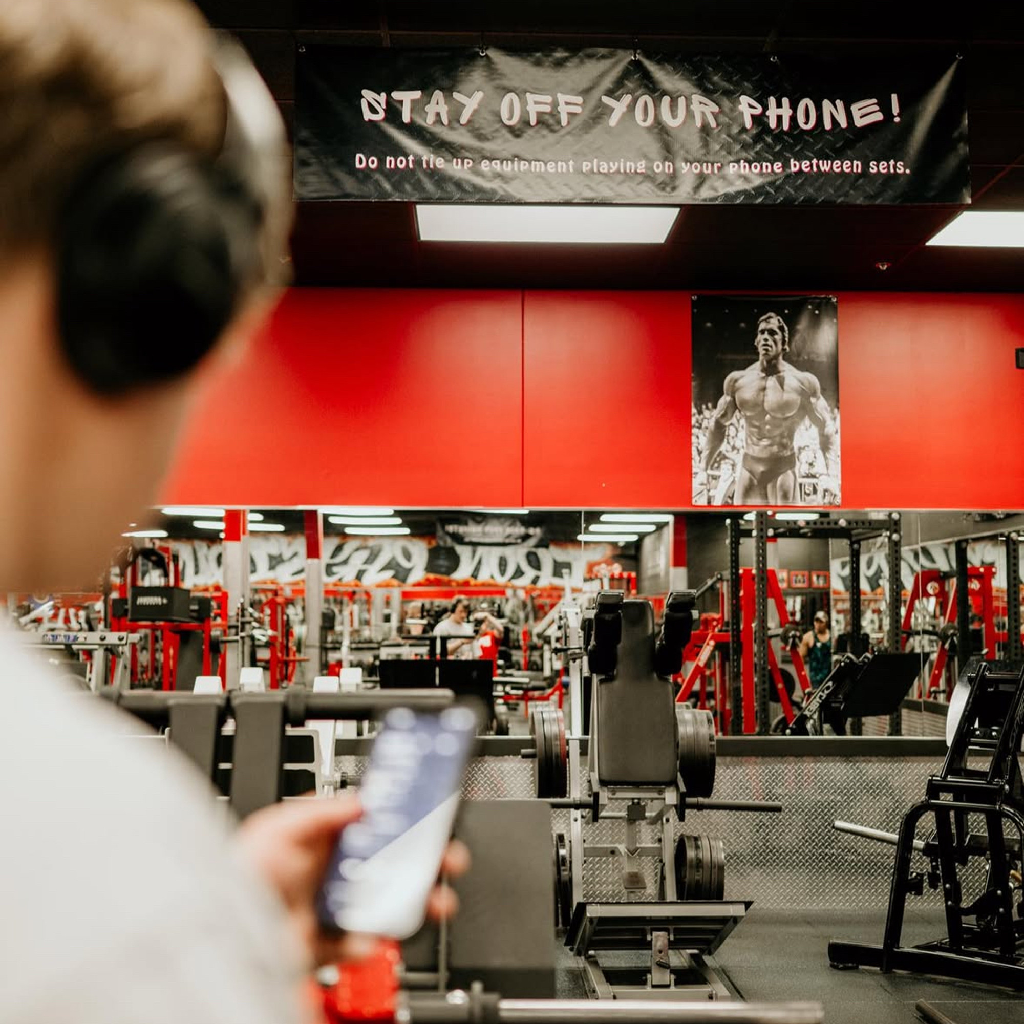 Iron Physique gym culture wall — Arnold Schwarzenegger poster watching over the weight room